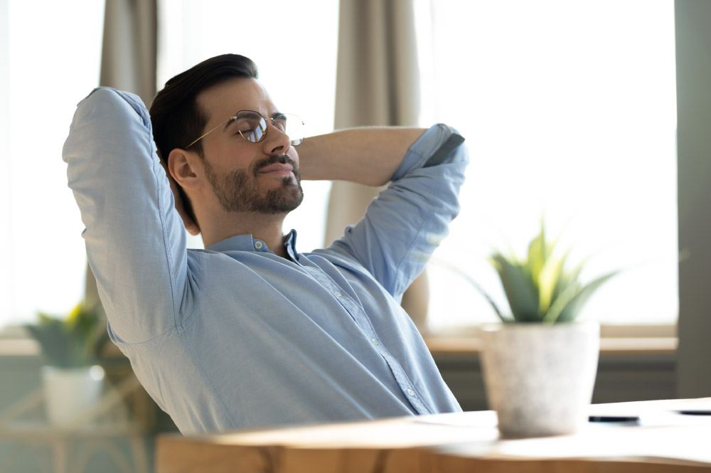 Peaceful young man daydreaming, leaning back, sitting at table