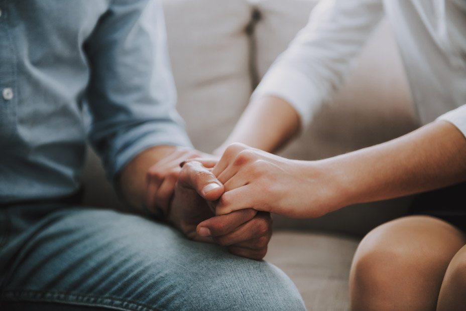 close-up of mixed-race couple holding hands in counseling session