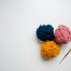 Three balls of yarn, pink, blue and yellow, and a crochet hook