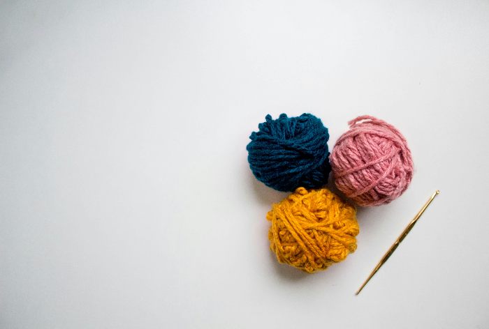 Three balls of yarn, pink, blue and yellow, and a crochet hook